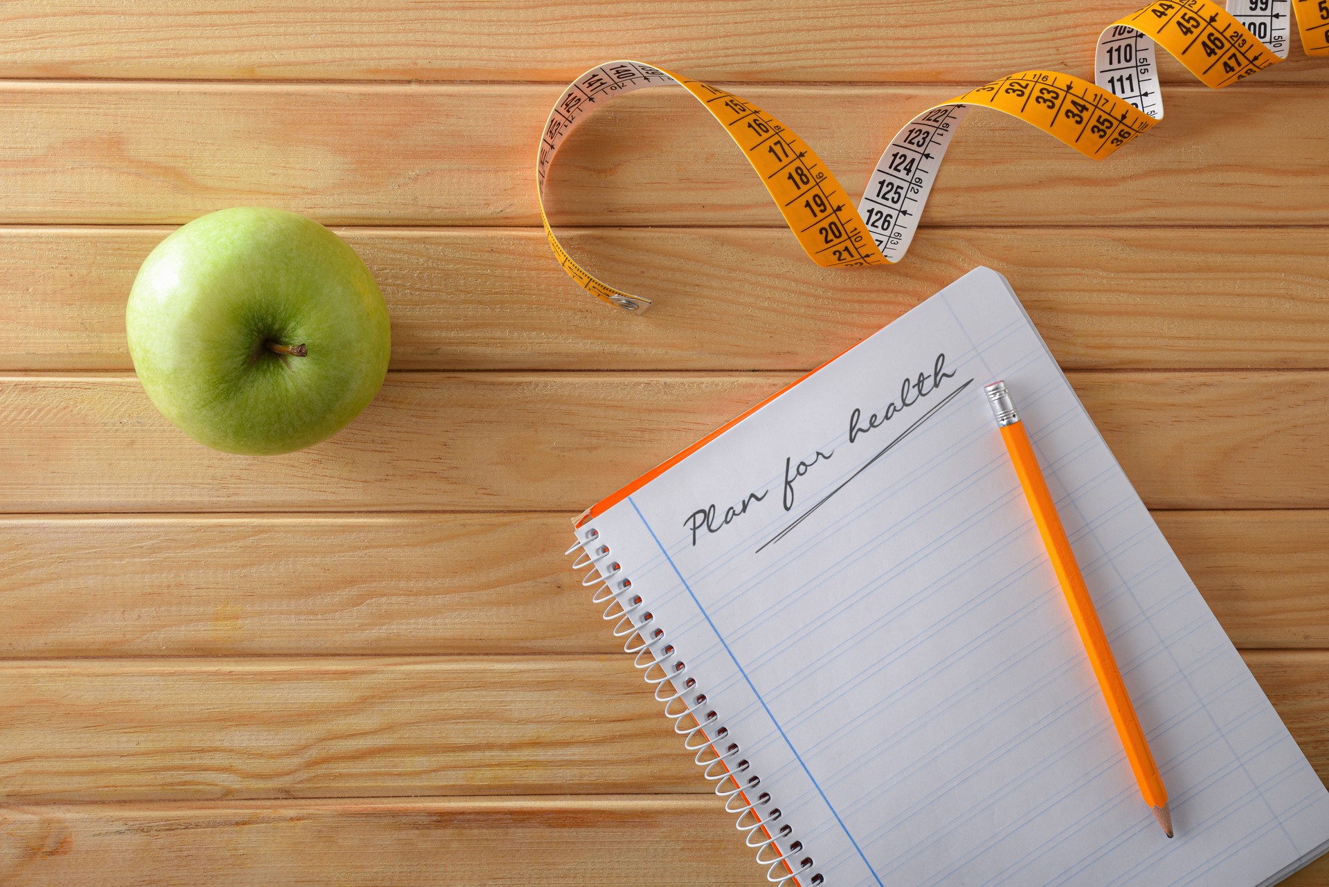 Health plan with apple notebook and tape measure top view